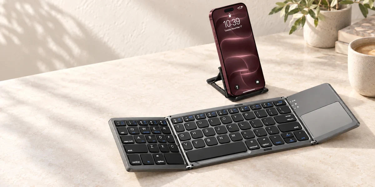 Gray folding wireless keyboard open beside a phone on a small stand.